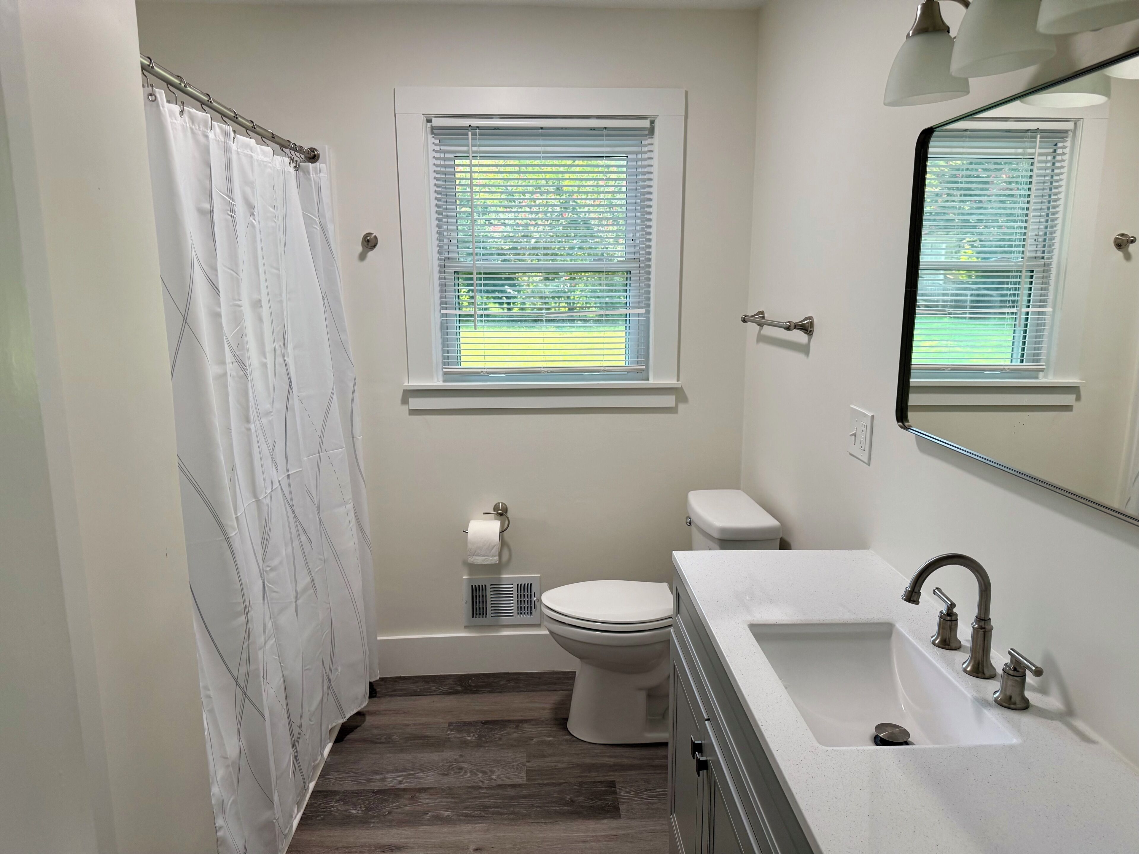 Une salle de bain avec un rideau de douche, des toilettes, une fenêtre et un lavabo.