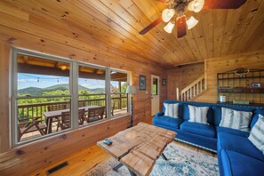Interior d'una cabana de fusta amb una finestra gran, un sofà blau i una taula de café de fusta.