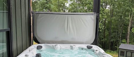 A hot tub with a wooden deck and a view of trees.