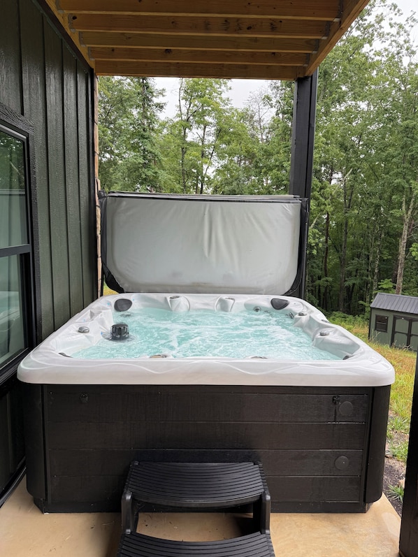 A hot tub with a wooden deck and a view of trees.