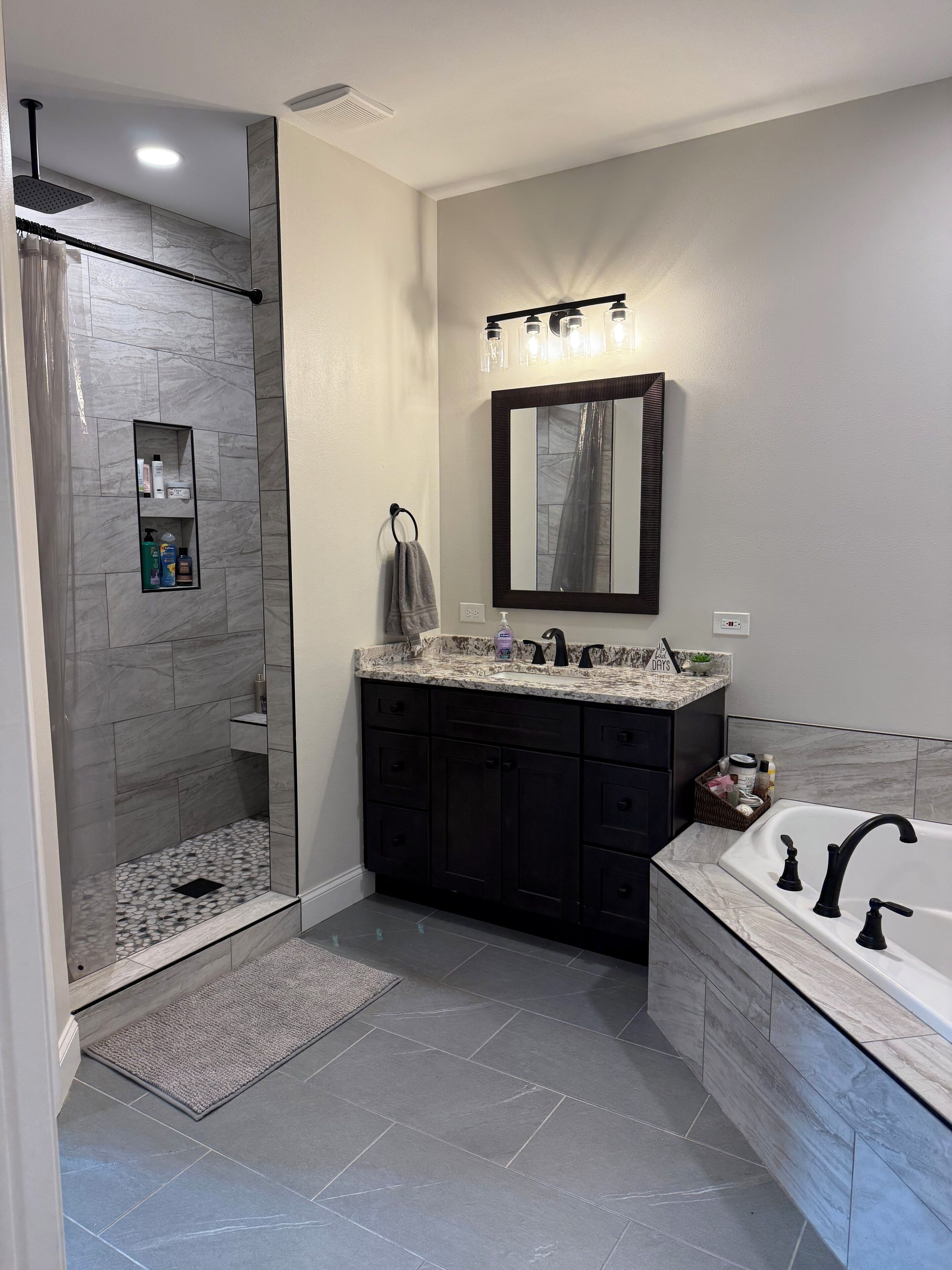 A modern bathroom with a walk-in shower, dark cabinetry, a large mirror, and a bathtub.