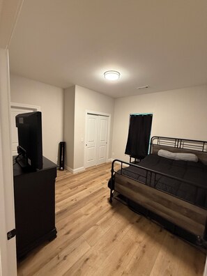 A bedroom with a bed, a dresser, a television, and a door.