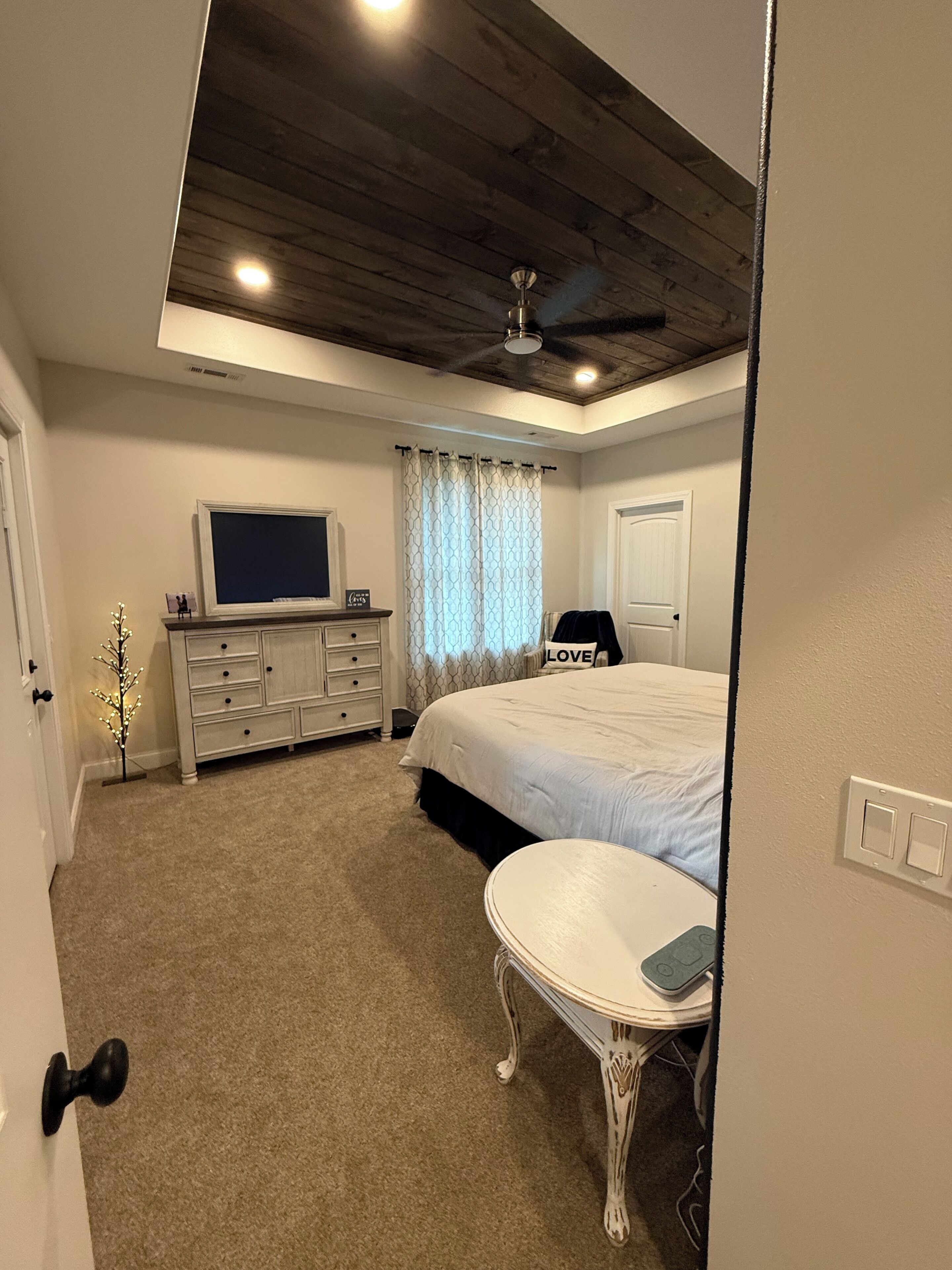 Une chambre à coucher comprenant un lit, une commode, un téléviseur, un ventilateur de plafond et une petite table.