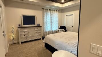 Une chambre à coucher comprenant un lit, une commode, un téléviseur, un ventilateur de plafond et une petite table.