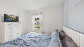 A bedroom with a bed, a dresser, a television on top of the dresser, and a window with curtains. - Owl's Head Haven 235-4 Bed House-Unfurnished (Freeport)