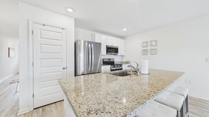 A kitchen with white cabinets, stainless steel appliances, granite countertops, and a white door. - Owl's Head Haven 235-4 Bed House-Unfurnished (Freeport)