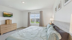 A bedroom with a bed, a bedside table with a lamp, a TV on the wall, and a window with curtains. - Owl's Head Haven 235-4 Bed House-Unfurnished (Freeport)