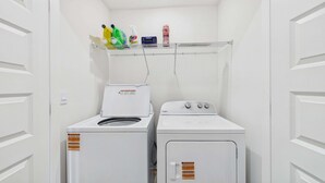A laundry room with two white Whirlpool washers and a metal shelf above holding cleaning supplies. - Owl's Head Haven 235-4 Bed House-Unfurnished (Freeport)
