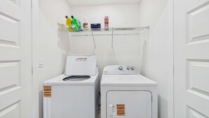 A laundry room with two white Whirlpool washers and a metal shelf above holding cleaning supplies. - Owl's Head Haven 235-4 Bed House-Unfurnished (Freeport)