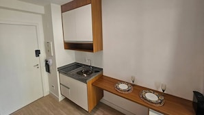 A compact kitchen with a built-in stove, a wooden countertop, and a small dining area with a table and chairs. - Apartamento com varanda - Pinheiros (São Paulo)