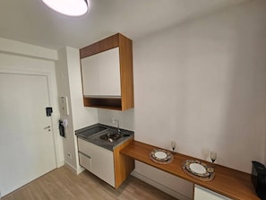 A compact kitchen with a built-in stove, a wooden countertop, and a small dining area with a table and chairs. - Apartamento com varanda - Pinheiros (São Paulo)