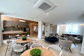 Un moderno vestíbulo de hotel con zona de comedor, arreglos de asientos y cocina al fondo.
