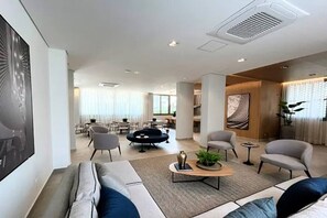 Ein modernes Wohnzimmer mit einer Couch, Sesseln, einem Couchtisch und einem Essbereich im Hintergrund.