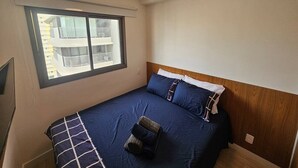 A bedroom with a bed, a window, and a wall-mounted TV. - Apartamento com varanda - Pinheiros (São Paulo)
