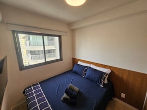 A bedroom with a bed, a window, and a wall-mounted TV. - Apartamento com varanda - Pinheiros (São Paulo)