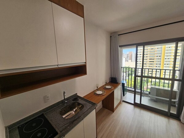 Una cocina moderna con estufa integrada, un fregadero y un pequeño comedor con vista a un balcón.