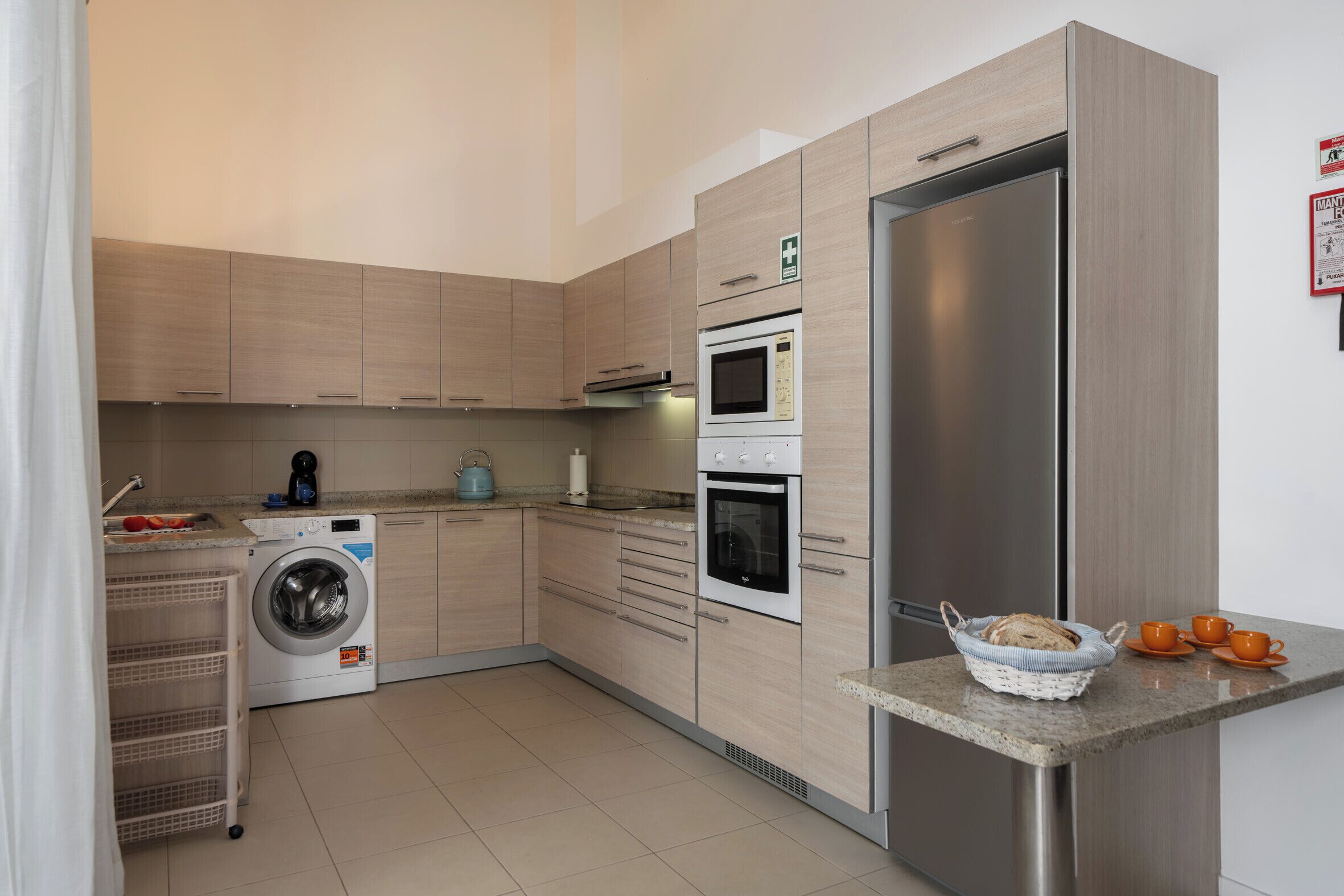 Una cocina moderna con refrigerador de acero inoxidable, horno empotrado, microondas y lavadora.