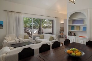 A modern living room with a dining area, large windows, and a view of palm trees.