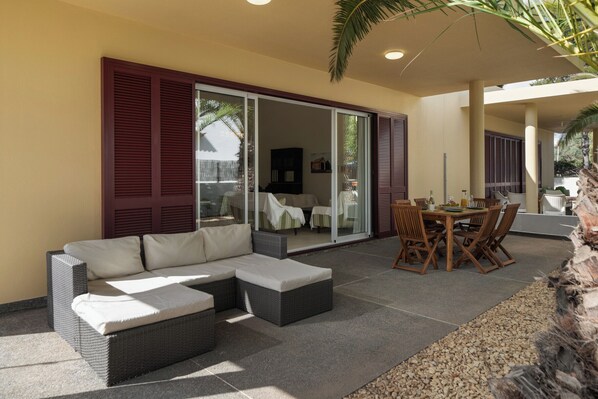 A patio area with a sectional sofa, a dining table with chairs, and a sliding glass door leading to an indoor space.