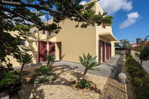 A modern two-story building with a beige facade, red shutters, and a gravel pathway leading to the entrance.