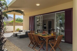 Un área de comedor al aire libre con una mesa y sillas, un sofá y vistas a la cocina a través de puertas de vidrio.