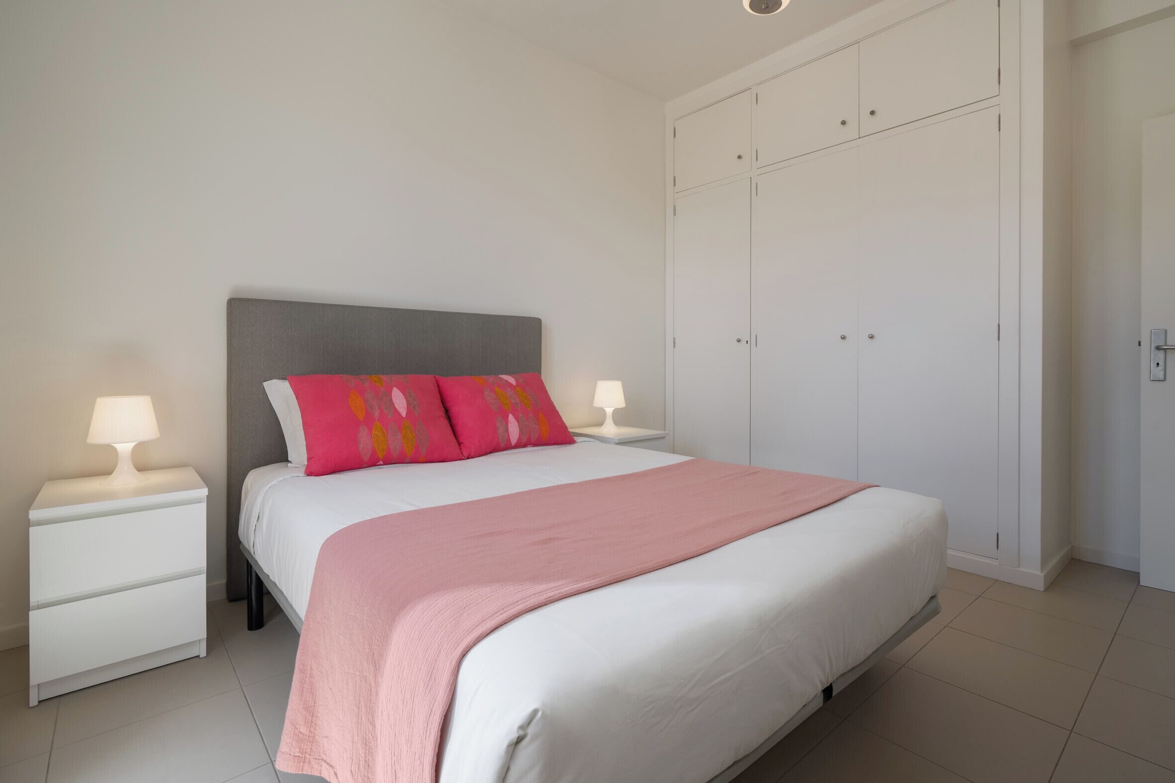Un dormitorio con cama, mesitas de noche, un armario y una lámpara en el techo.