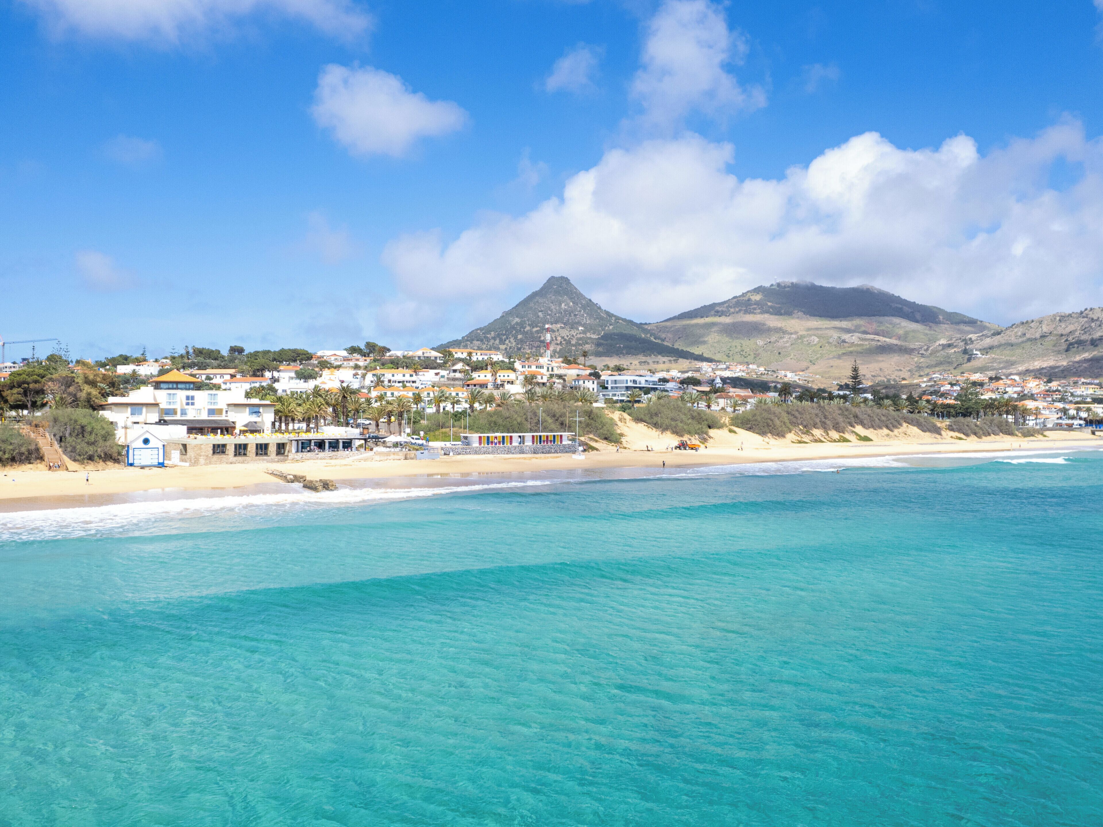 Un pueblo costero con edificios a lo largo de la playa, aguas turquesas cristalinas y una montaña al fondo.