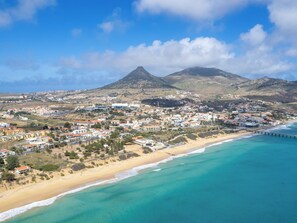 Une ville côtière avec une plage, une montagne en arrière-plan et une jetée qui s’avance dans la mer.