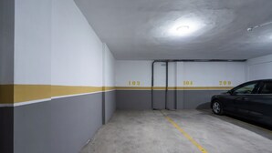 A parking garage with numbered parking spaces, a car parked in space 104, and a yellow line on the floor. - Palmier • 1BR avec balcon & parking (Casablanca)