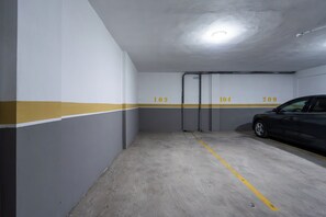 A parking garage with numbered parking spaces, a car parked in space 104, and a yellow line on the floor. - Palmier • 1BR avec balcon & parking (Casablanca)