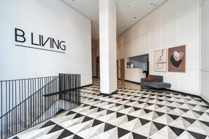 A modern interior with a geometric patterned floor, a staircase with metal railings, and a wall with the text 'B L I V I N G'. - Palmier • 1BR avec balcon & parking (Casablanca)
