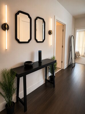 Un couloir moderne avec un plancher en bois foncé, une console noire sur laquelle est posé un vase noir, deux miroirs fixés au mur et deux appliques murales.