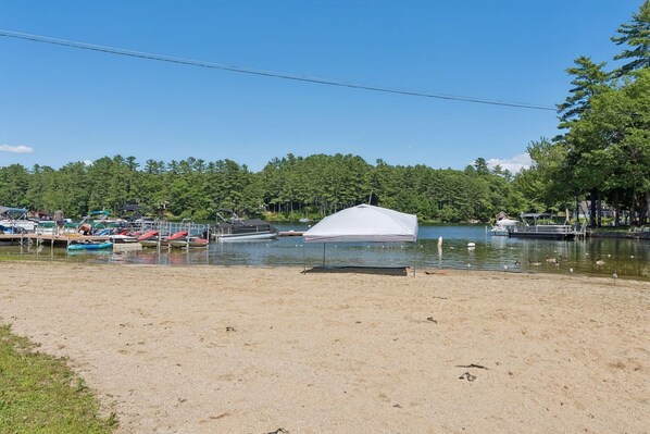 A lakeside area with a tent, boats, and a sandy beach.