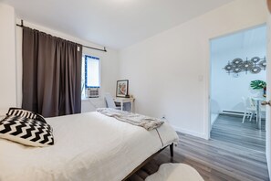 Ein Schlafzimmer mit Bett, Schreibtisch und Stuhl. Es gibt ein Fenster mit Vorhängen, eine Tür zu einem Balkon und eine Wanddekoration.