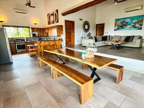 A spacious living area with a wooden dining table, benches, a sofa, and a coffee table. - Sunset Villa Macaw, 2 King Suites, Pool & Ocean View (Manuel Antonio)