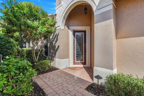 A building entrance with a brick pathway leading to a door with a glass panel. - Private Pool Villa | Players Club & Spa | Golf Views (Naples)