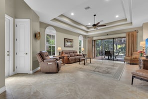 A spacious living room with a ceiling fan, a large window with curtains, and a view of the outdoors. - Private Pool Villa | Players Club & Spa | Golf Views (Naples)