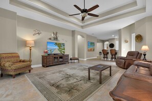 A spacious living room with a ceiling fan, a large flat-screen TV, a wooden cabinet, and a patterned rug. - Private Pool Villa | Players Club & Spa | Golf Views (Naples)