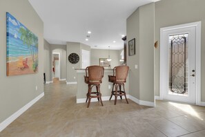 A hallway with two wicker chairs, a clock, and a painting of a beach scene. - Private Pool Villa | Players Club & Spa | Golf Views (Naples)