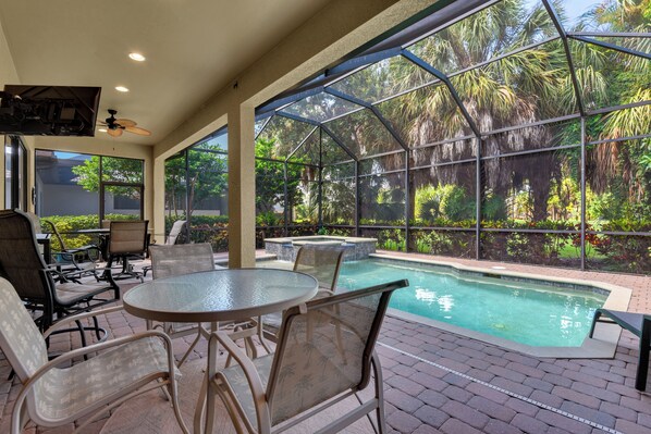 An outdoor pool area with a glass enclosure, surrounded by chairs and tables. - Private Pool Villa | Players Club & Spa | Golf Views (Naples)