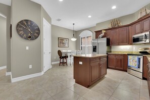 A kitchen with a central island, wooden cabinets, a stainless steel refrigerator, and a clock on the wall. - Private Pool Villa | Players Club & Spa | Golf Views (Naples)
