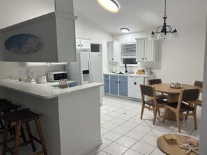 A modern kitchen with white cabinetry, a central island, and a dining area with wooden chairs. - elegant coastal retreat in a secure gated community at Panama City Beach  (Panama City)