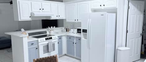 A modern kitchen with white cabinetry, a built-in oven, a refrigerator, and a dining area with a table and chairs.