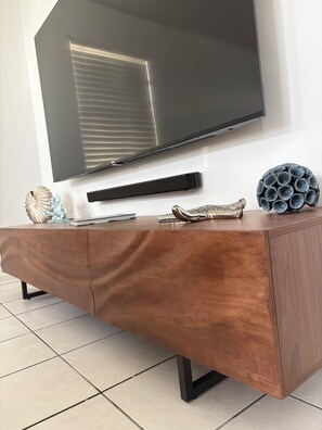 Ein modernes Wohnzimmer mit einem großen Flachbildfernseher an der Wand, einem Holztische mit Dekoration und einem gefliesten Boden.