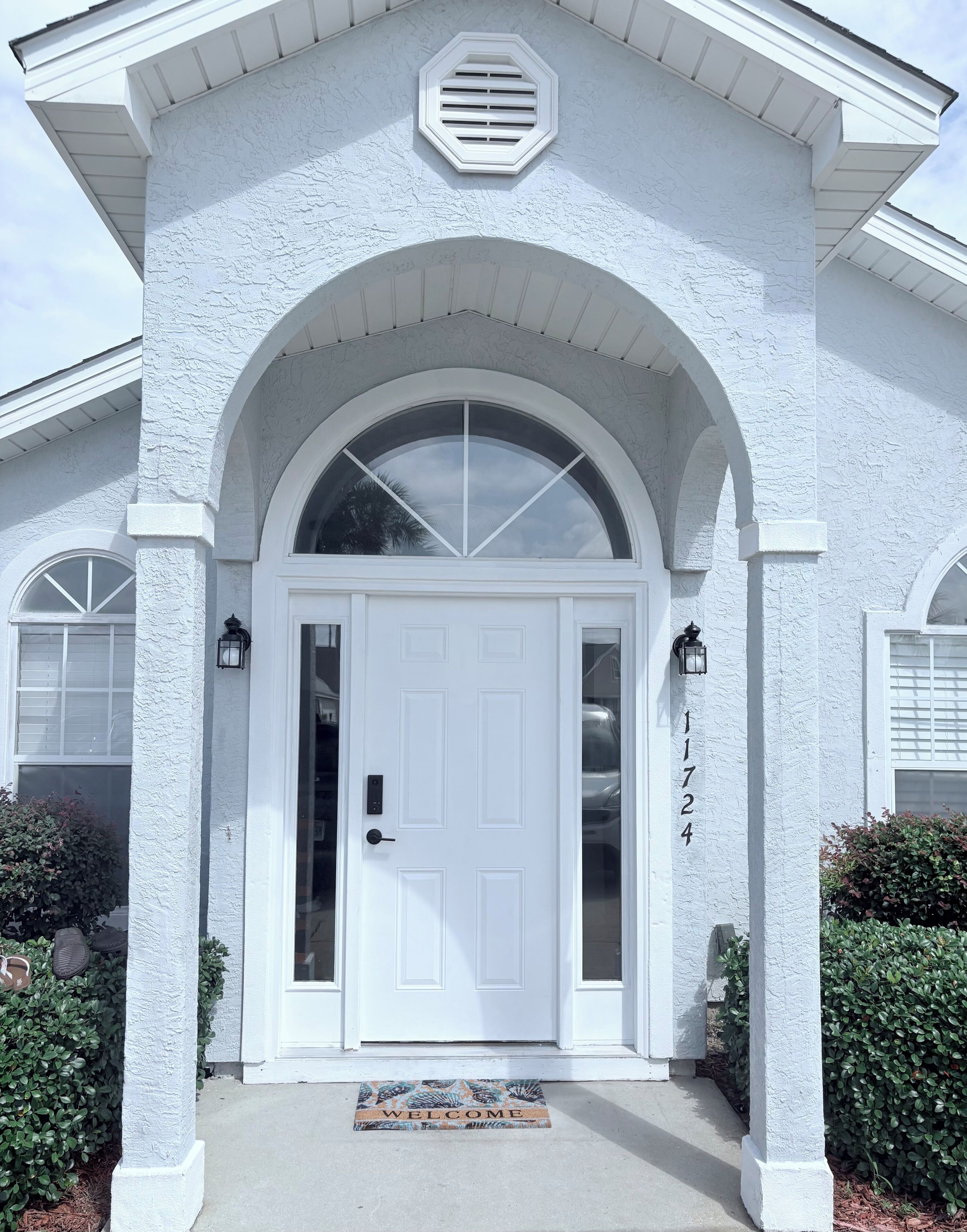 A white house with a large arched entrance, a number plaque, and a welcome mat.