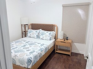 Ein Schlafzimmer mit einem hölzernen Bett, einem Nachttisch mit Lampe und einem Fenster mit Jalousie.