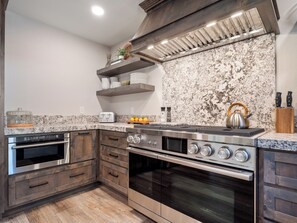 A modern kitchen with a stainless steel stove, oven, wooden cabinets, and a granite backsplash. - Gabriel Getaway | Mountain Comfort in Skyland, NV (Zephyr Cove)