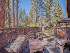 An outdoor deck with wicker furniture, a wooden fence, and a view of a forested area. - Gabriel Getaway | Mountain Comfort in Skyland, NV (Zephyr Cove)