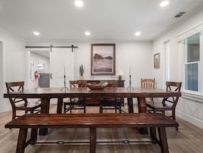 A dining room with a large wooden table, benches, and chairs. There is a painting on the wall, a window with a view, and a door leading to another room. - Gabriel Getaway | Mountain Comfort in Skyland, NV (Zephyr Cove)