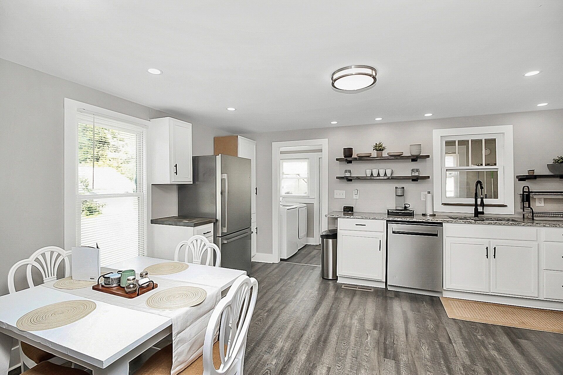 A modern kitchen with white cabinetry, a stainless steel refrigerator, and a dining area with a white table and chairs.